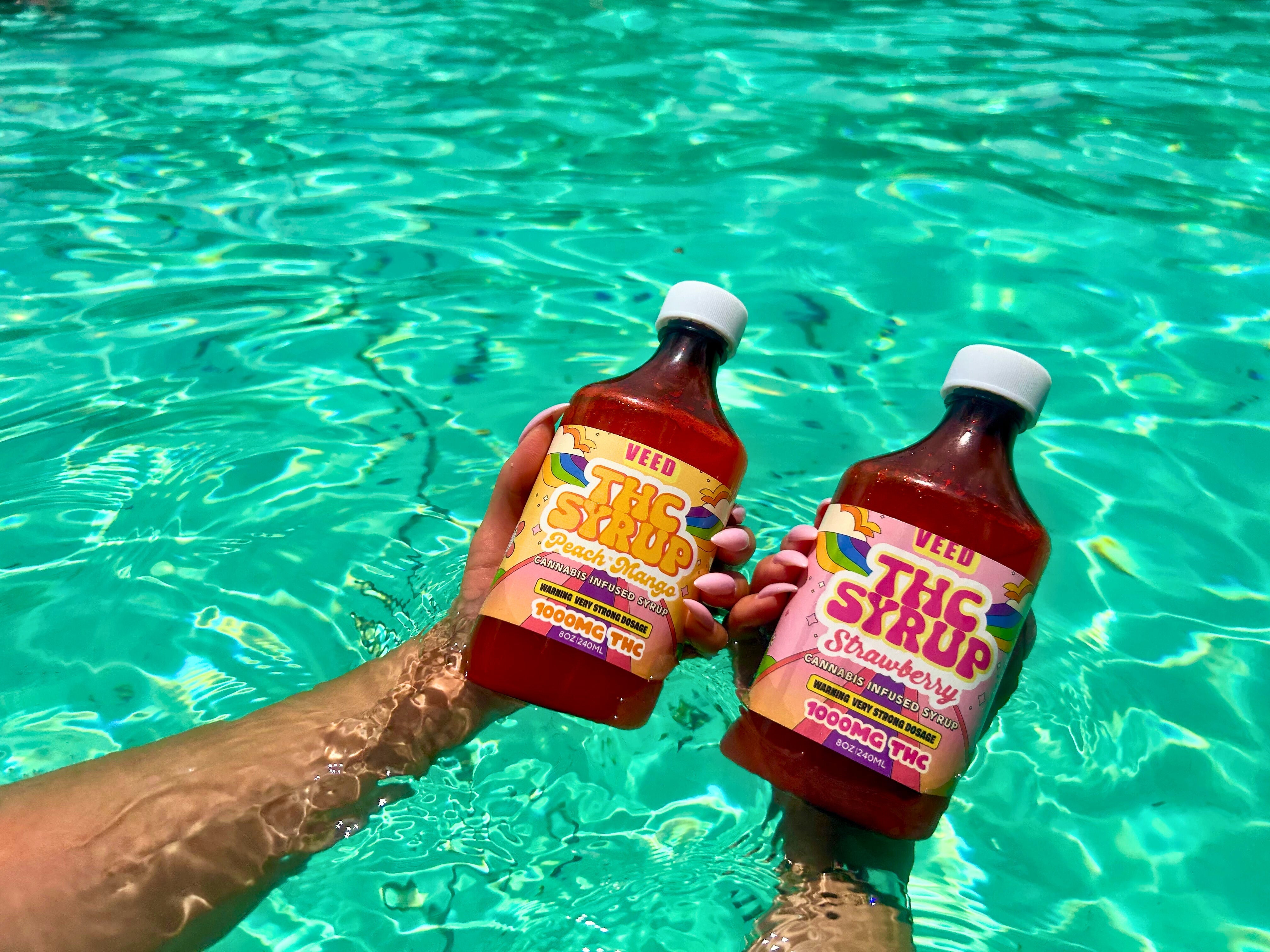 Two VEED Labs THC syrup bottles  held in someones hands in the pool on a sunny day