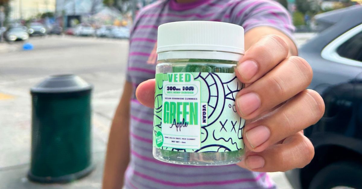 Person holding VEED Labs THC 10MG Gummies container in green apple flavor.