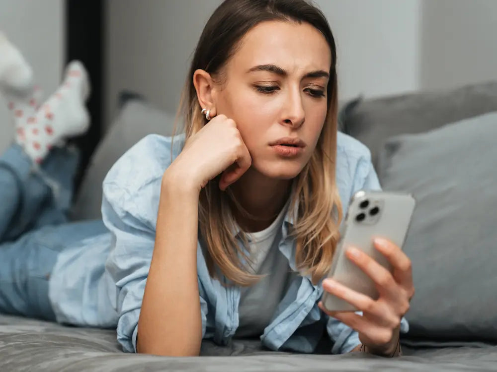 Concerned woman looking at her phone while lying on a bed, symbolizing uncertainty around mixing THC gummies with cold medicine like NyQuil
